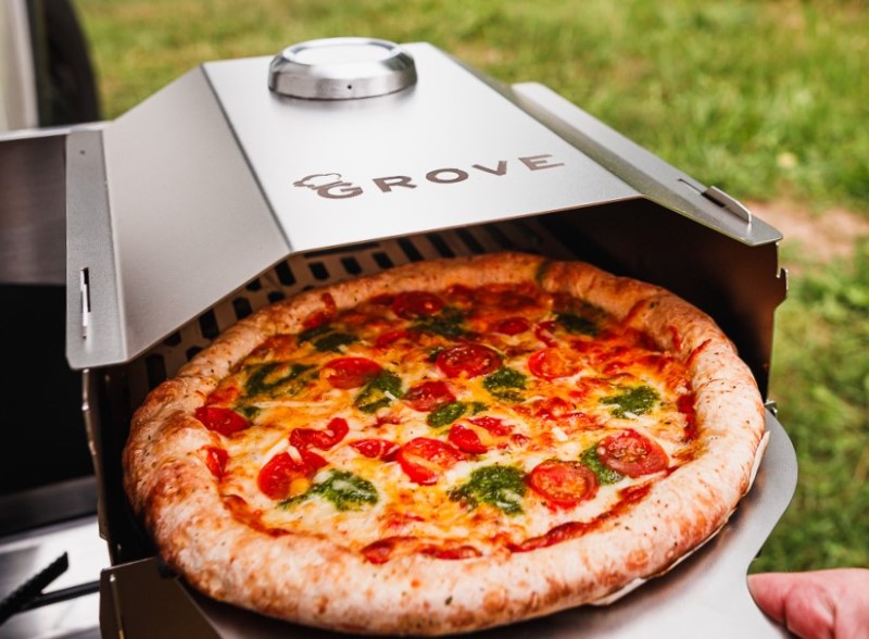 Ambientefoto:
Horst der multifunktionale Campingofen aus dem grade mit dem Grove Pizzaschieber eine Tiefkühlpizza herausgenommen wird