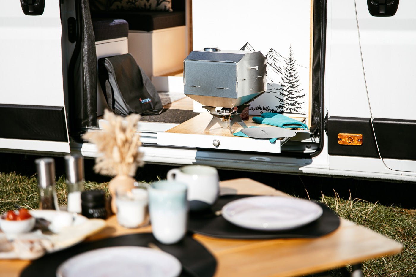 Ambientefoto:
Horst der multifunktionale Campingofen auf einem Außentisch eines Campers