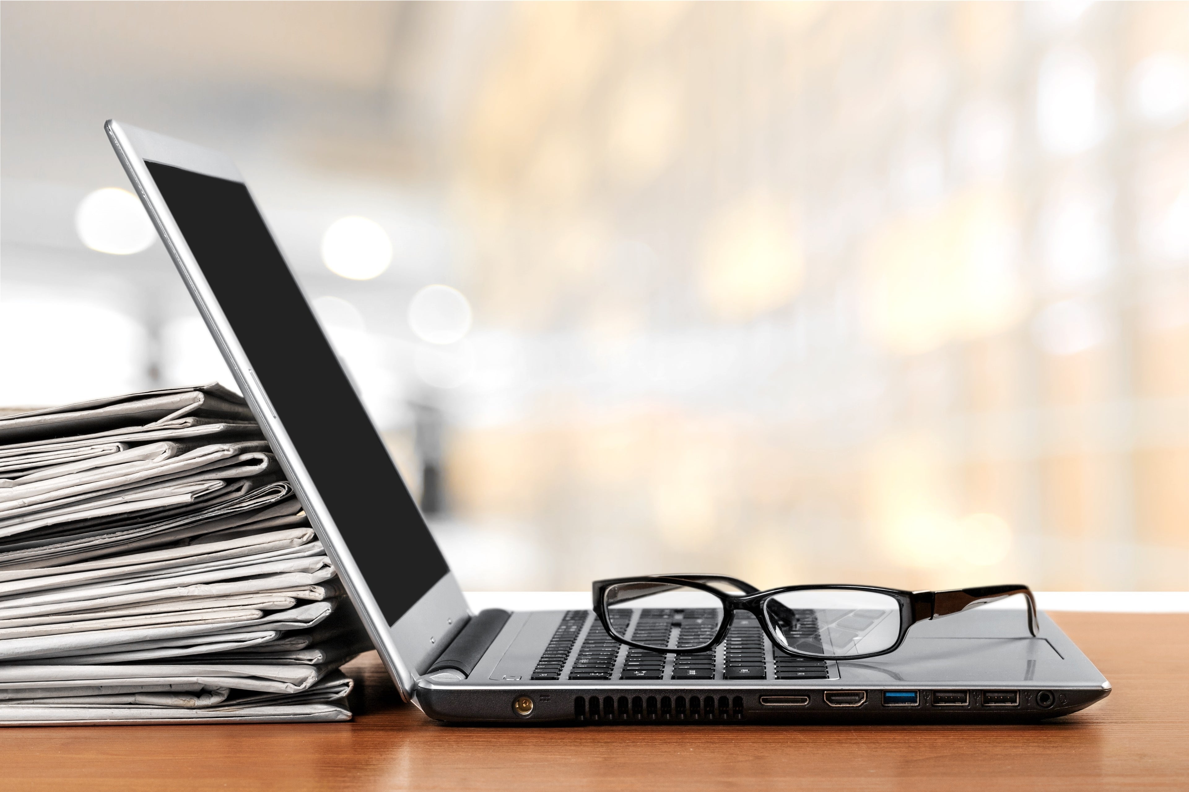 Headerbild:
Ein Laptop auf dem eine Brille liegt mit einem Stapel Zeitungen