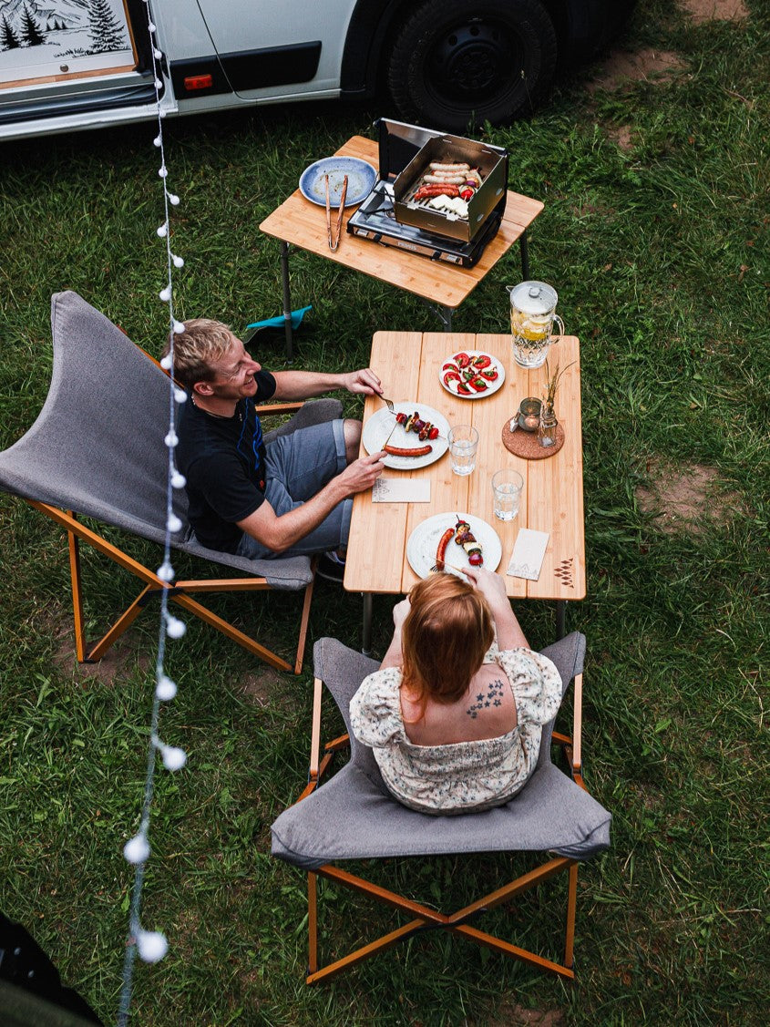 Grove Camping - Campingofen Horst als Gasgrill mit gedecktem Tisch und Personen die essen