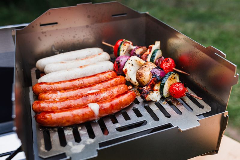 Ambientefoto:
Grove Camping - Horst der multifunktionale Campingofen als Gasgrill beim Grillen von Bratwürstchen